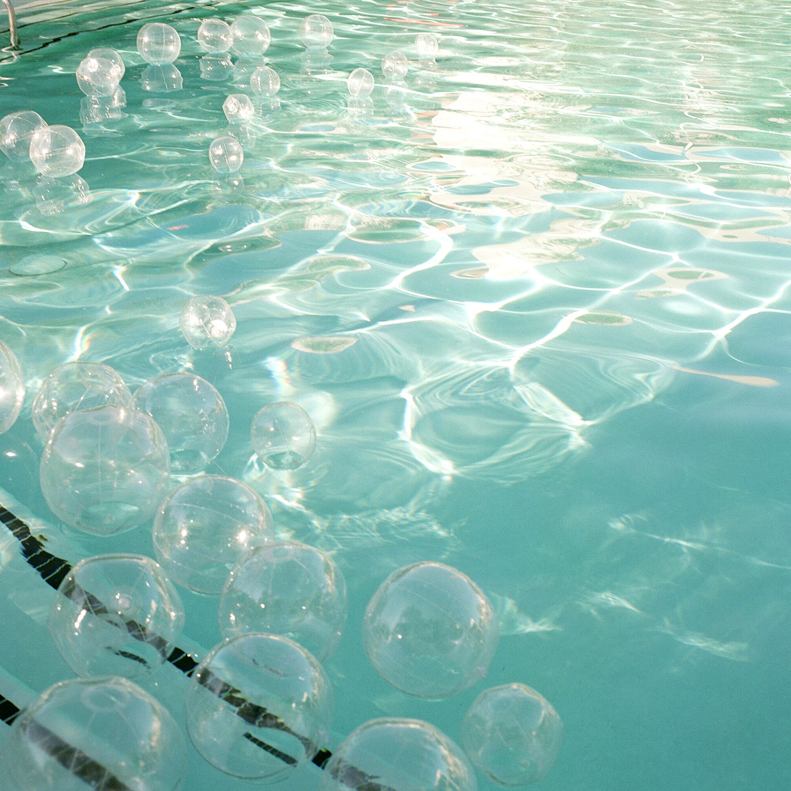 Close up shot of a pale turquoise swimming pool containing many clear beach balls that look like bubbles.
