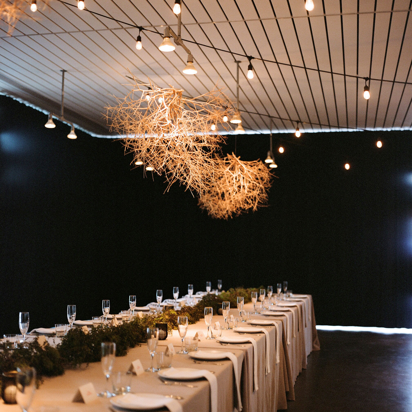 Extra wide shot of one of the long tables for guests where tumbleweeds collected for decoration over the tables with care. The tablecloths are a floor-length in natural flax linen with creosote garlands running down the center. This alternate shot is to show what the room looked like once it was dark. 