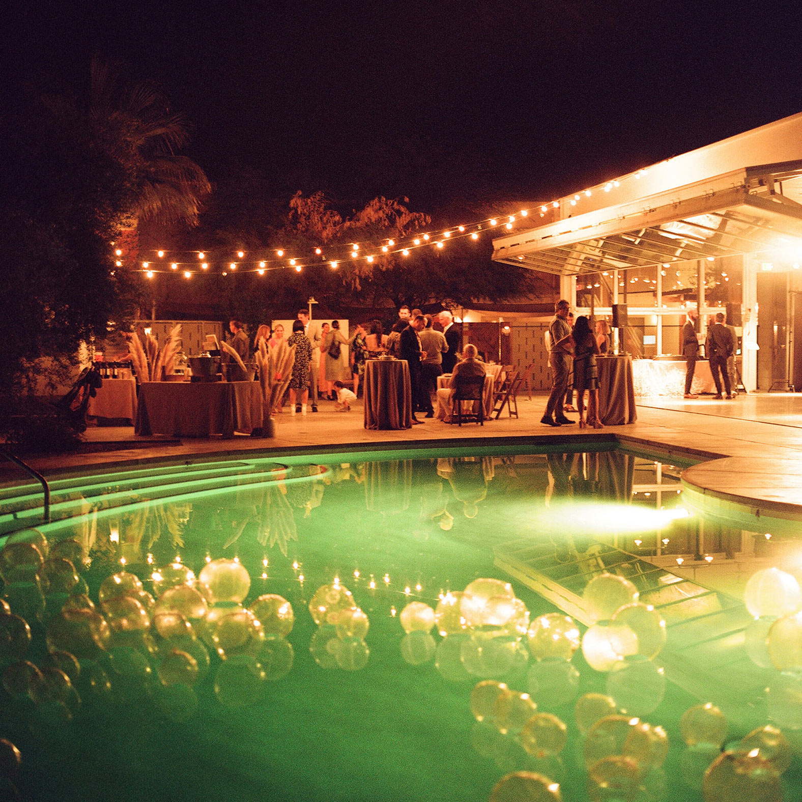 Wide shot of the pool with bubbles and the party goers socializing in the background. 