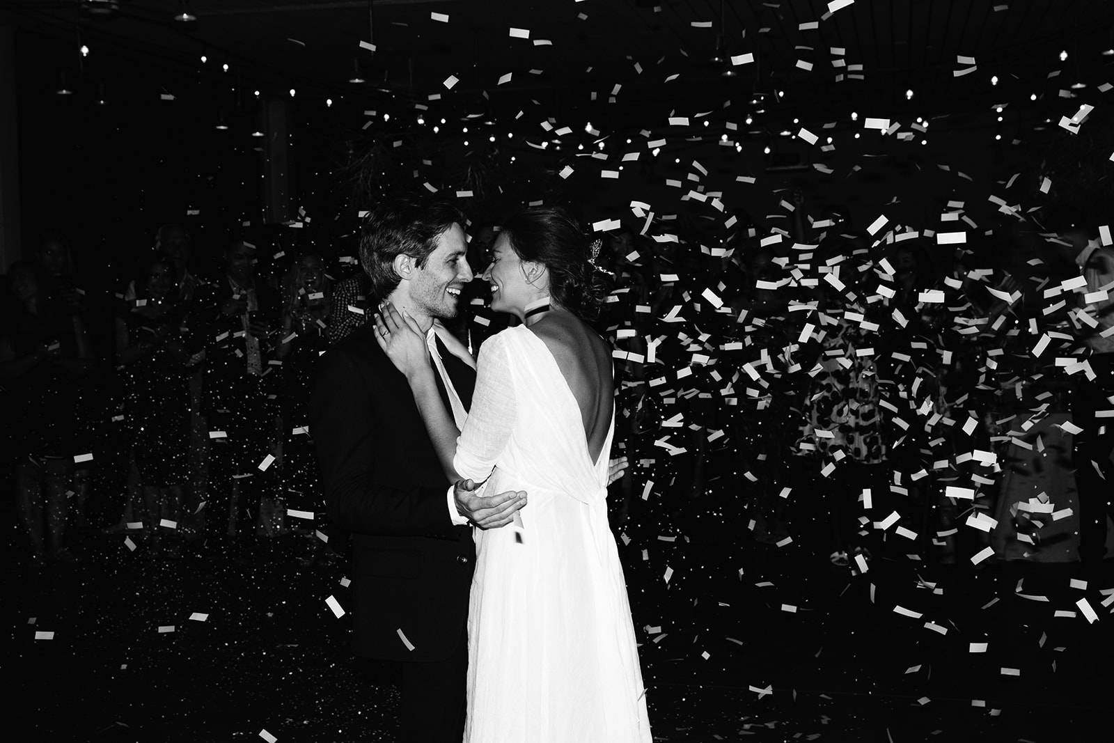 Black and white candid shot of K and E on the dance floor in an embrace with white paper confetti flying into the air.