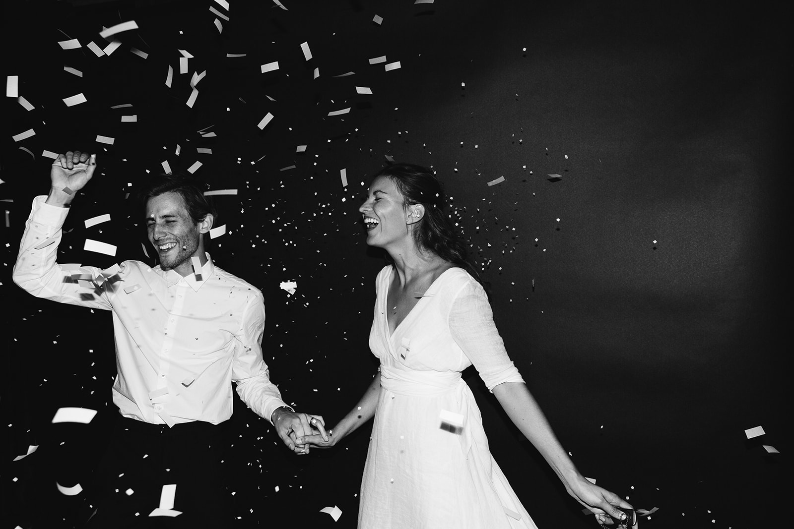 Final shot in black and white of K and E holding hands and smiling with their eyes both closed while white paper confetti flys into the air.