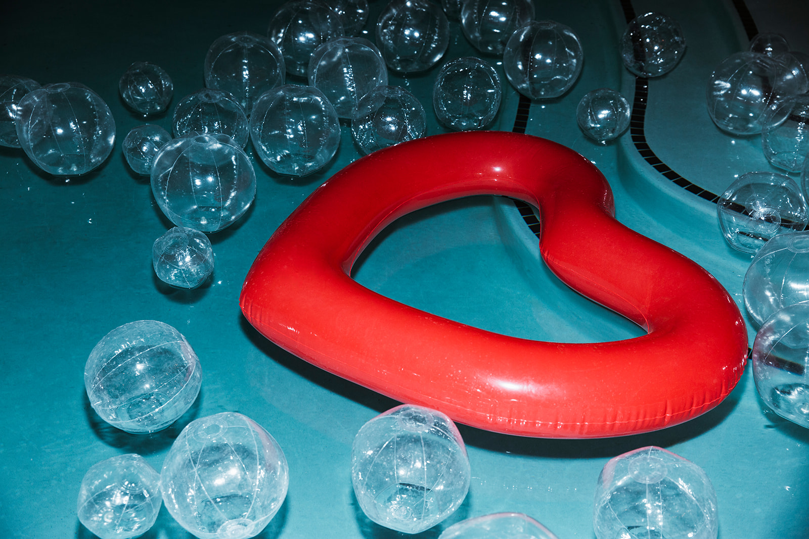 Close up shot of a heart shaped pool float surrounded by clear beach balls in multiple sizes giving the effect of bubbles.   