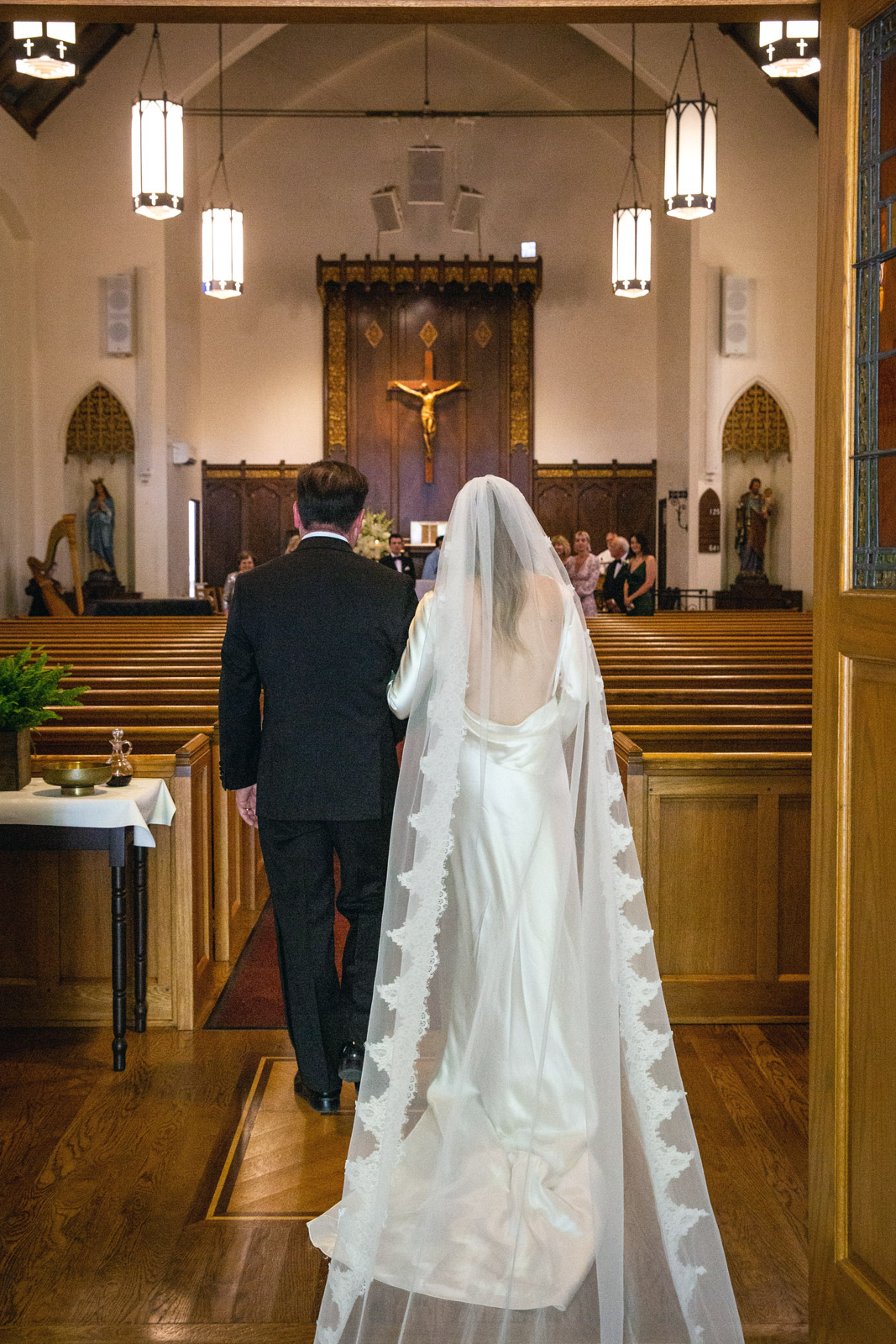 Wide shot of M and her dad with their backs to the camera walking down the aisle.