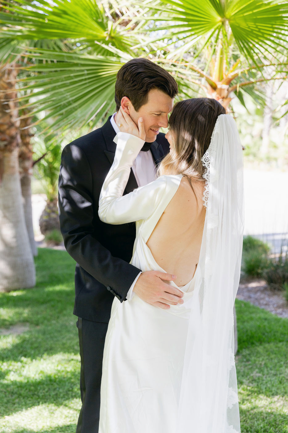 medium shot of the couple embracing looking away from camera with palm trees in the background.