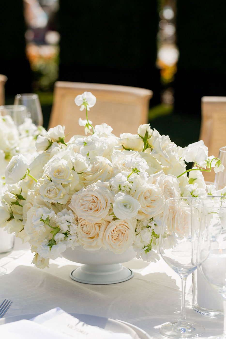 Close up shot of an all white flower centerpiece on a white tablecloth.