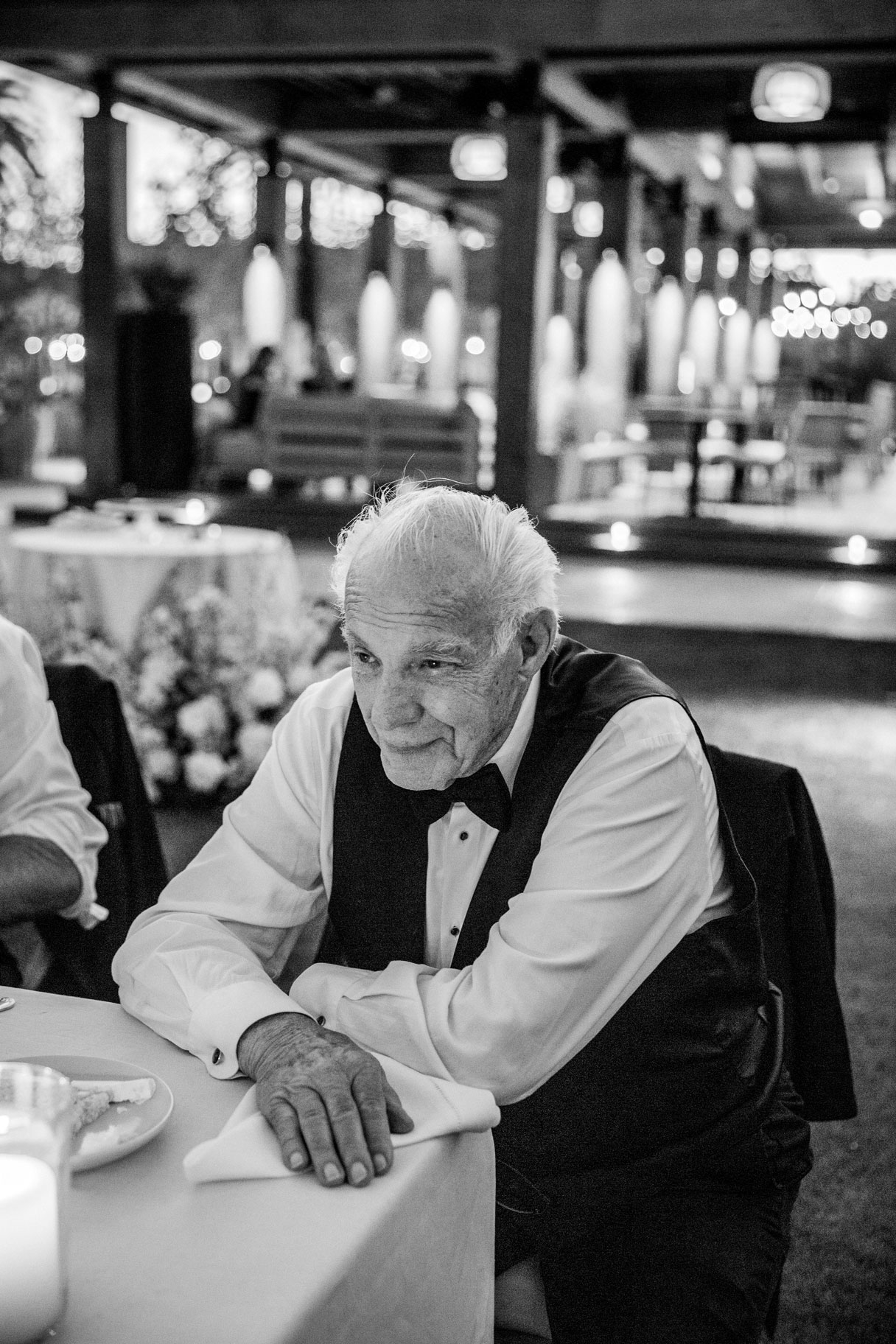 Black and white portrait of the grooms grandfather sitting at a table talking with guests.