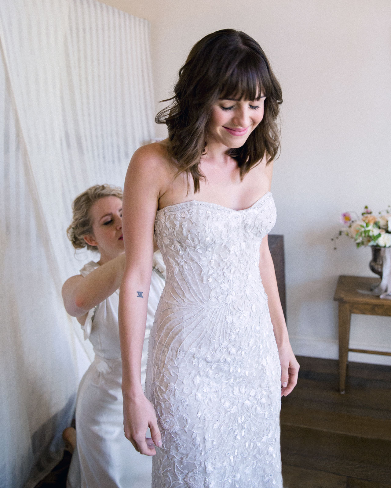 Medium shot of the bride getting help form her sister who is zipping up her dress.