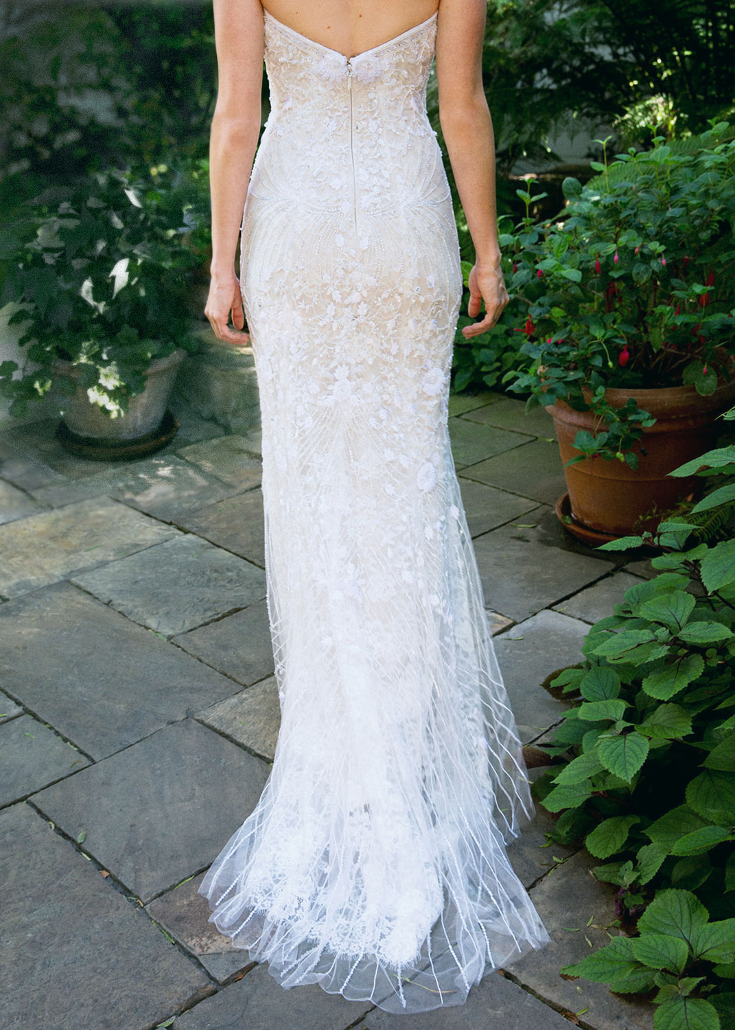 Close up shot of the back of the brides dress on a stone path with greenery all around her.