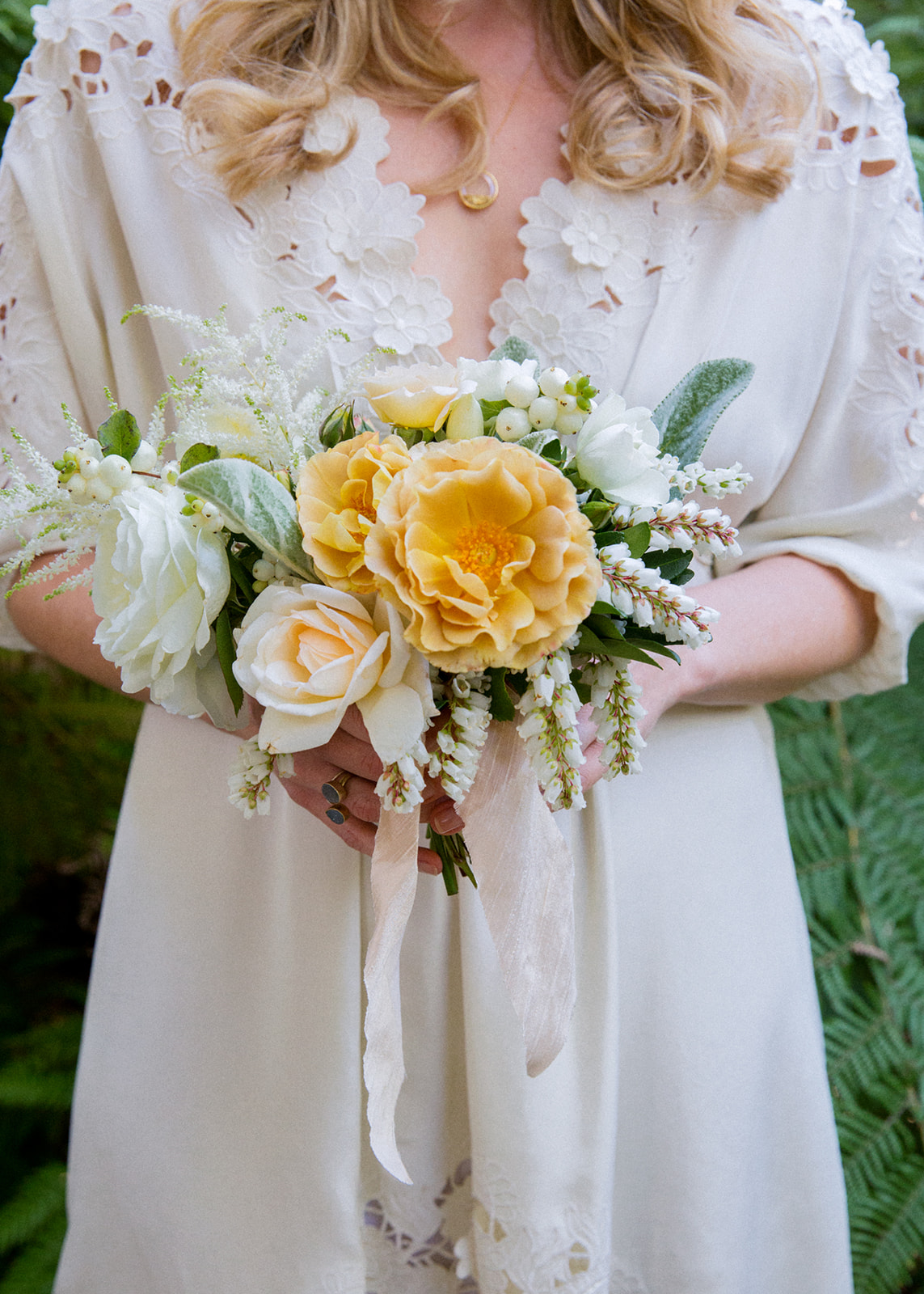 Close up shot of a bridesmaid holding a bouquet with 2 large dusty yellow roses in the center.