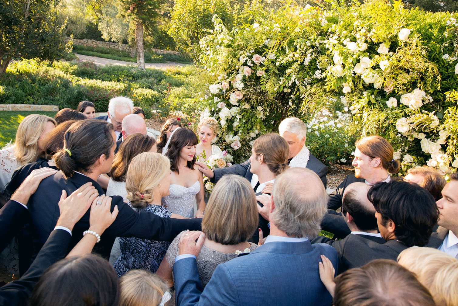 Wide shot of all of the guests at this wedding placing hands on each other while praying for the couple.