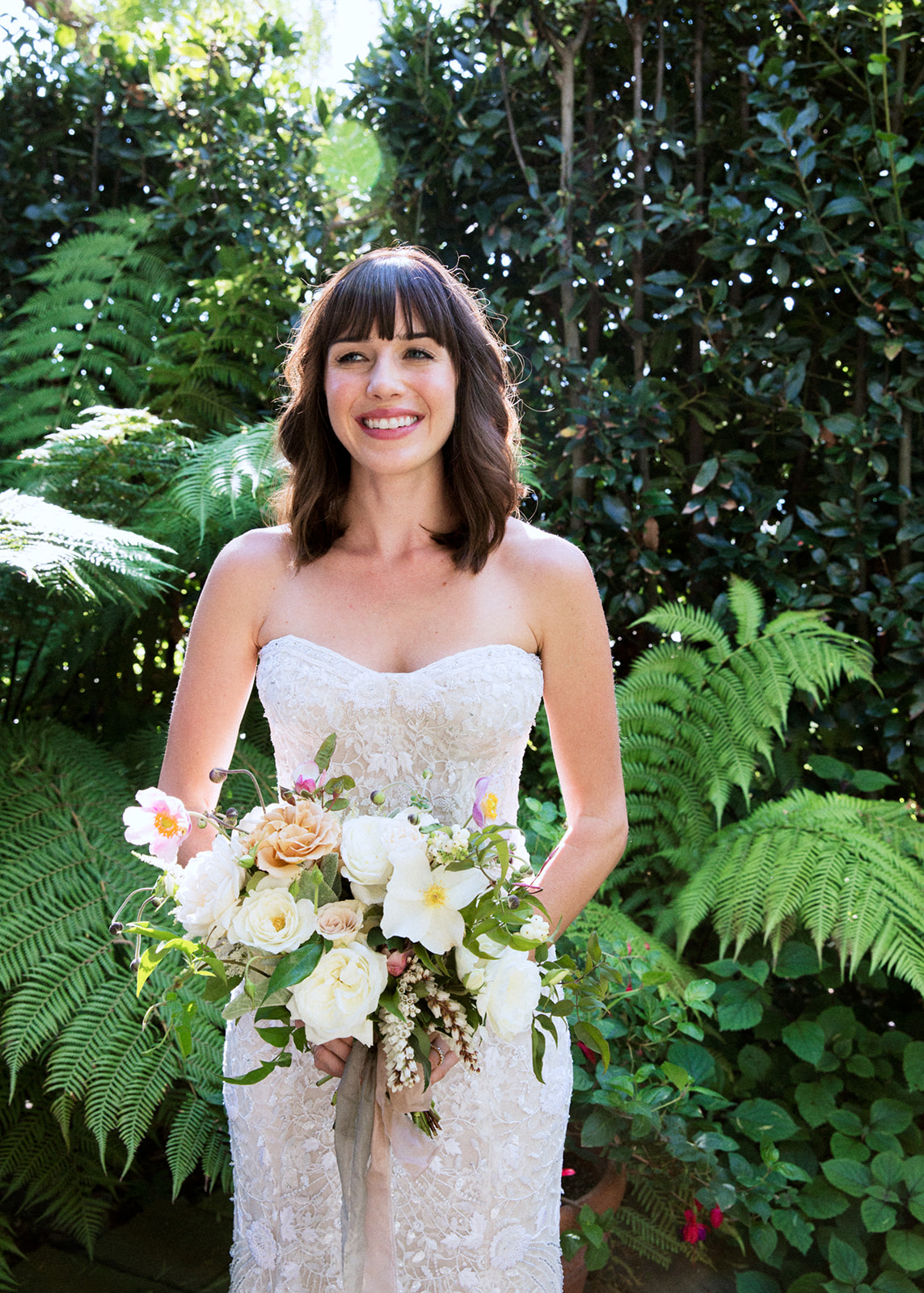 Medium shot of the bride holding her bouquet with ferns in the background.