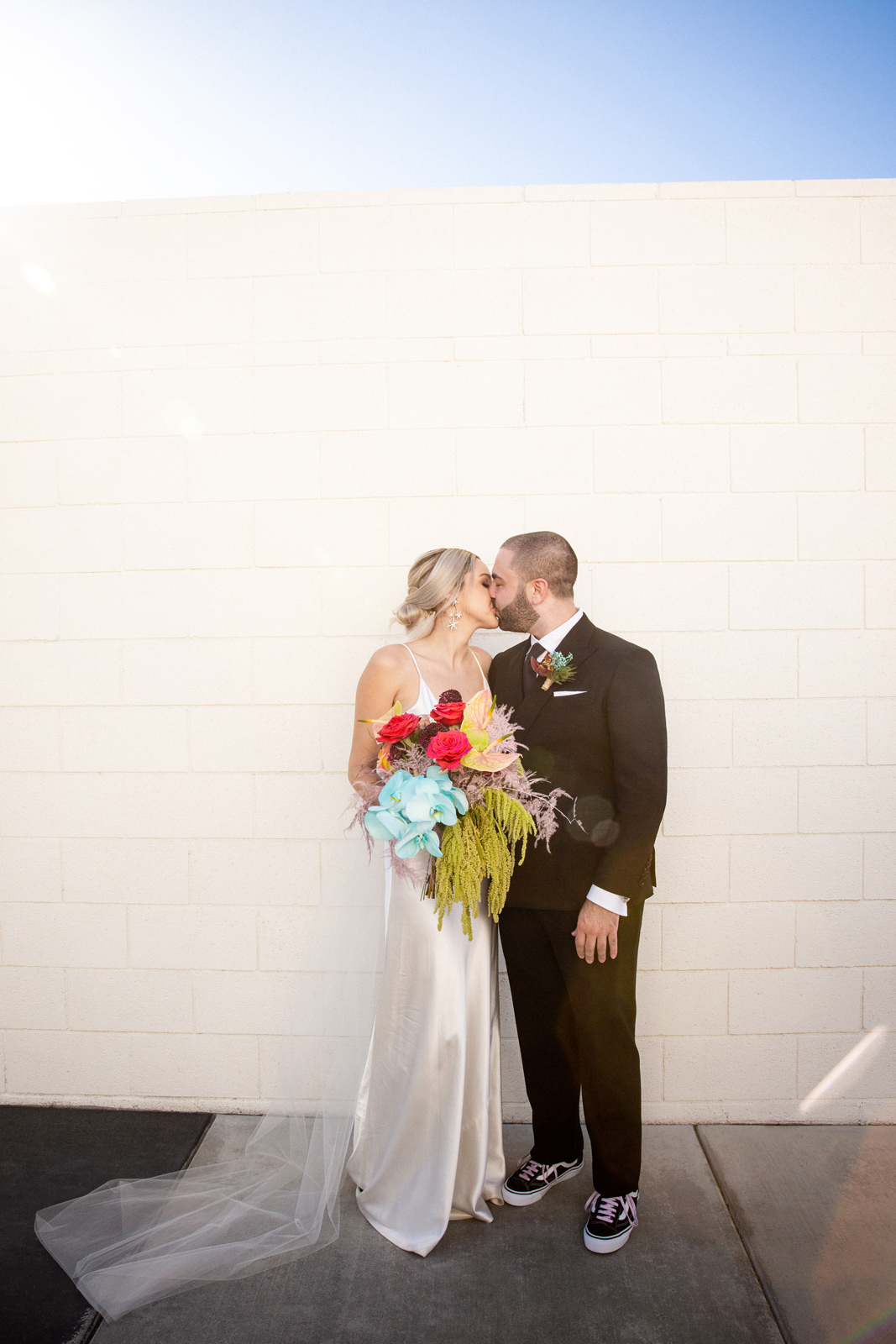 Wide shot of the couple kissing with a sun flare coming in at the camera