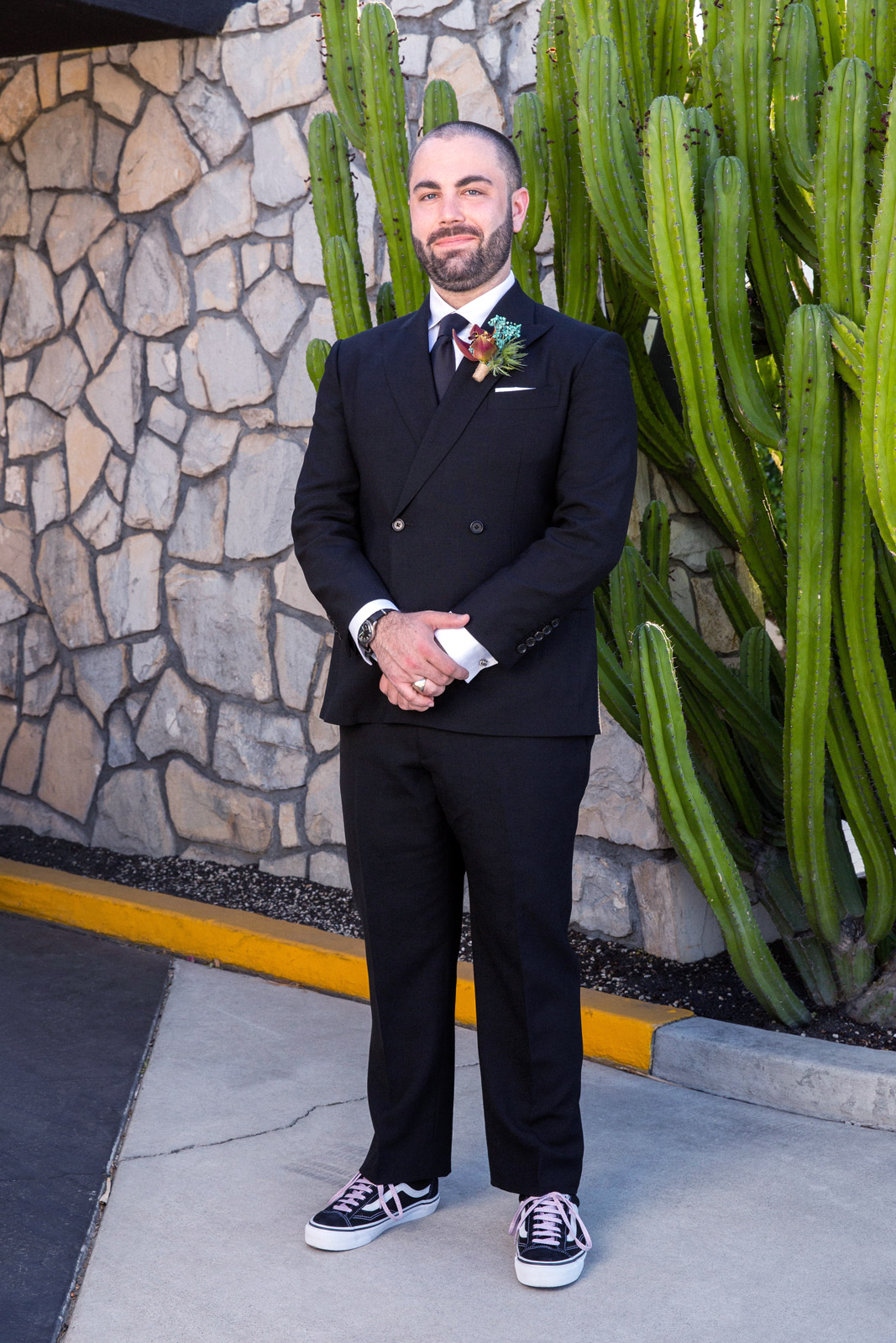 Wide portrait of B standing in front a stone wall and tall cactus.