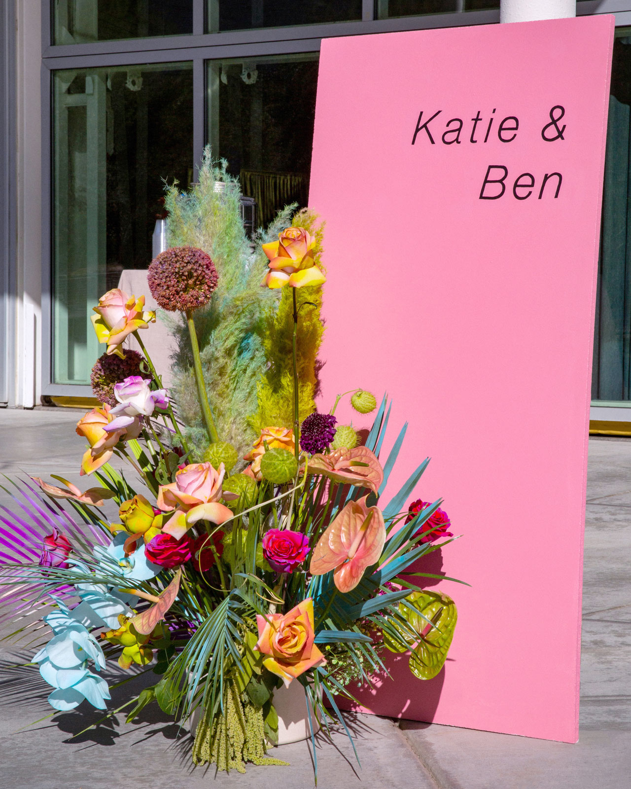Wide shot of a pink sign stating "K and B" with a large vase of colorful flowers.