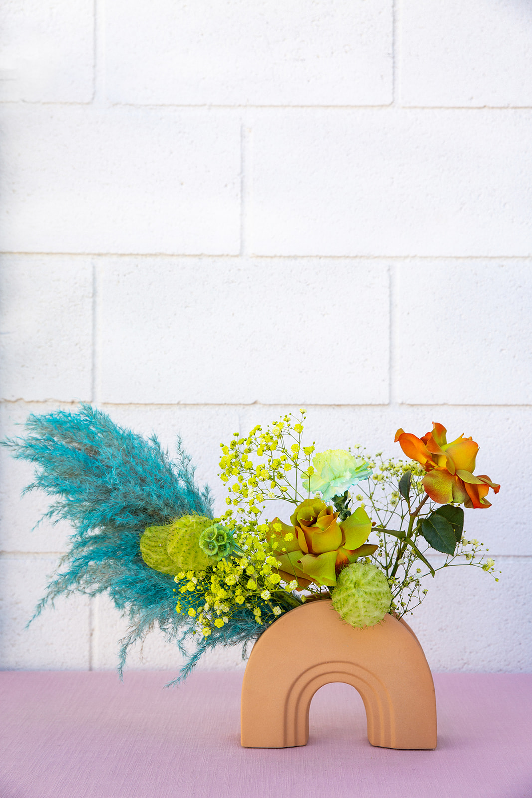 Close up of a floral center piece. This one was shot outside on a pink piece of material and against a white brick wall. The arrangement mimics the brides bouquet in the colors and boldness with the vessel itself was made of terracotta.