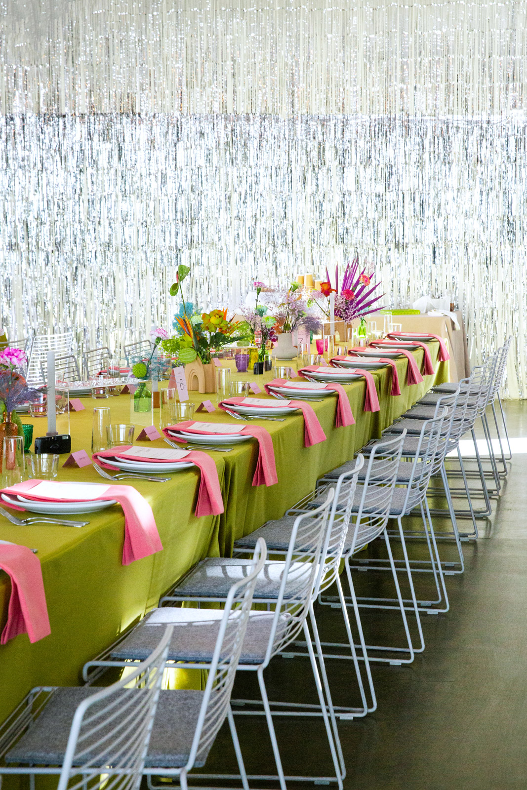 Wide shot in front of a metallic wall of one of the long tables the guests sat in for the reception. The table clothes were a green velvet with pink cotton napkins.