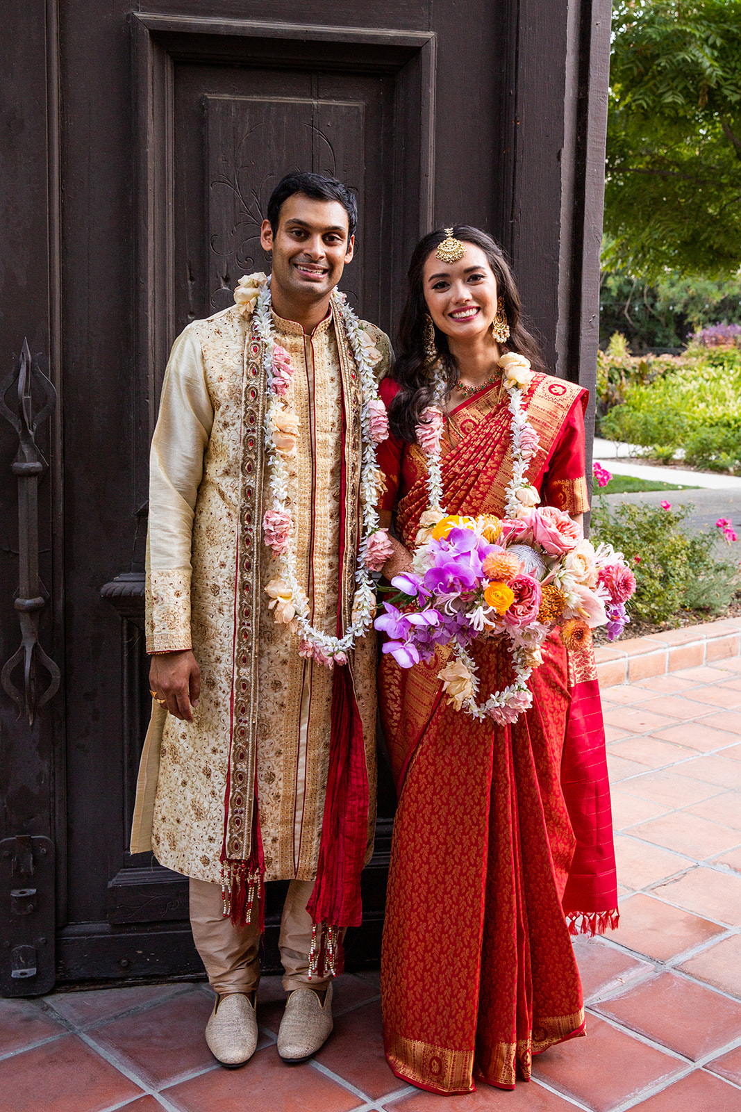 Wide full-body shot of our couple posed in front of a large, ornate, dark wooden door.