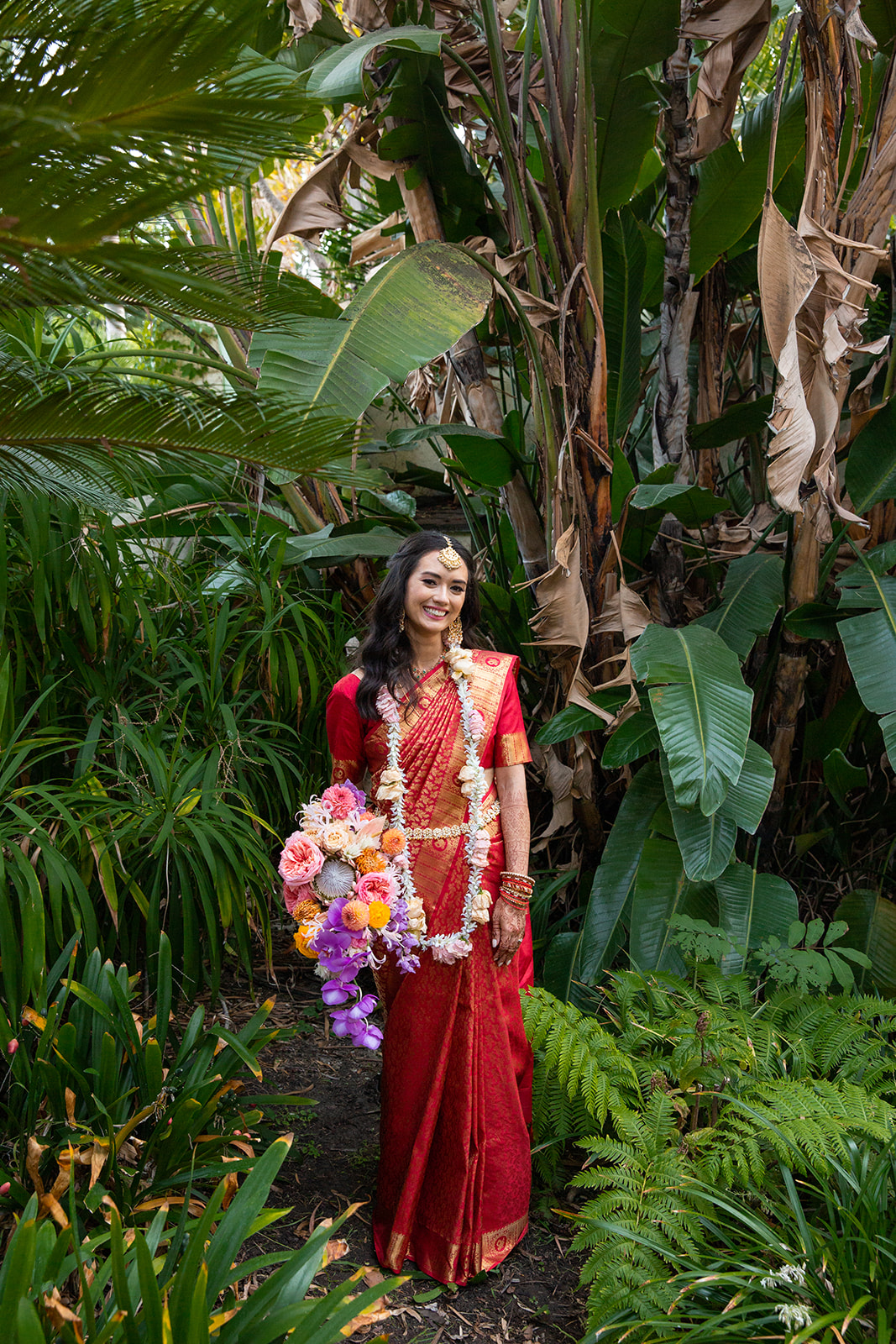 Fullbody portrait of A in the lush green setting smiling at camera.