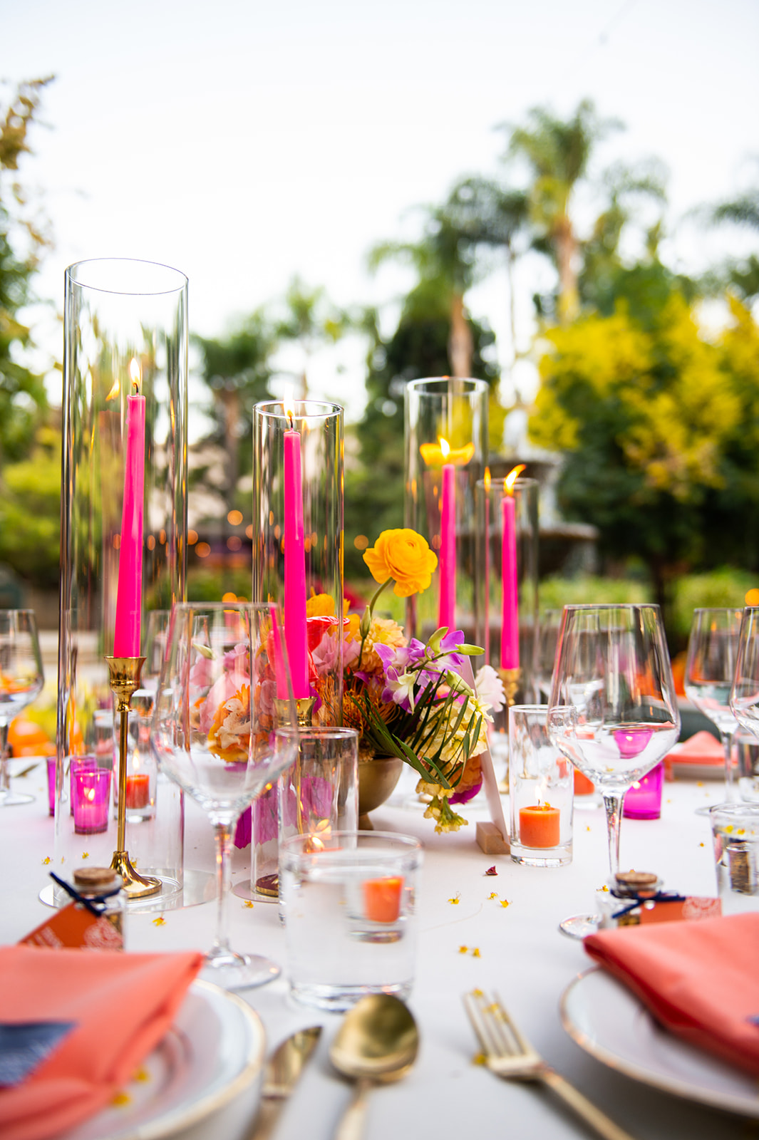 Close-up shot of the reception tables. It’s colorful with bright pink candlesticks, orange votive candles in little glass vases, and gold cutlery.