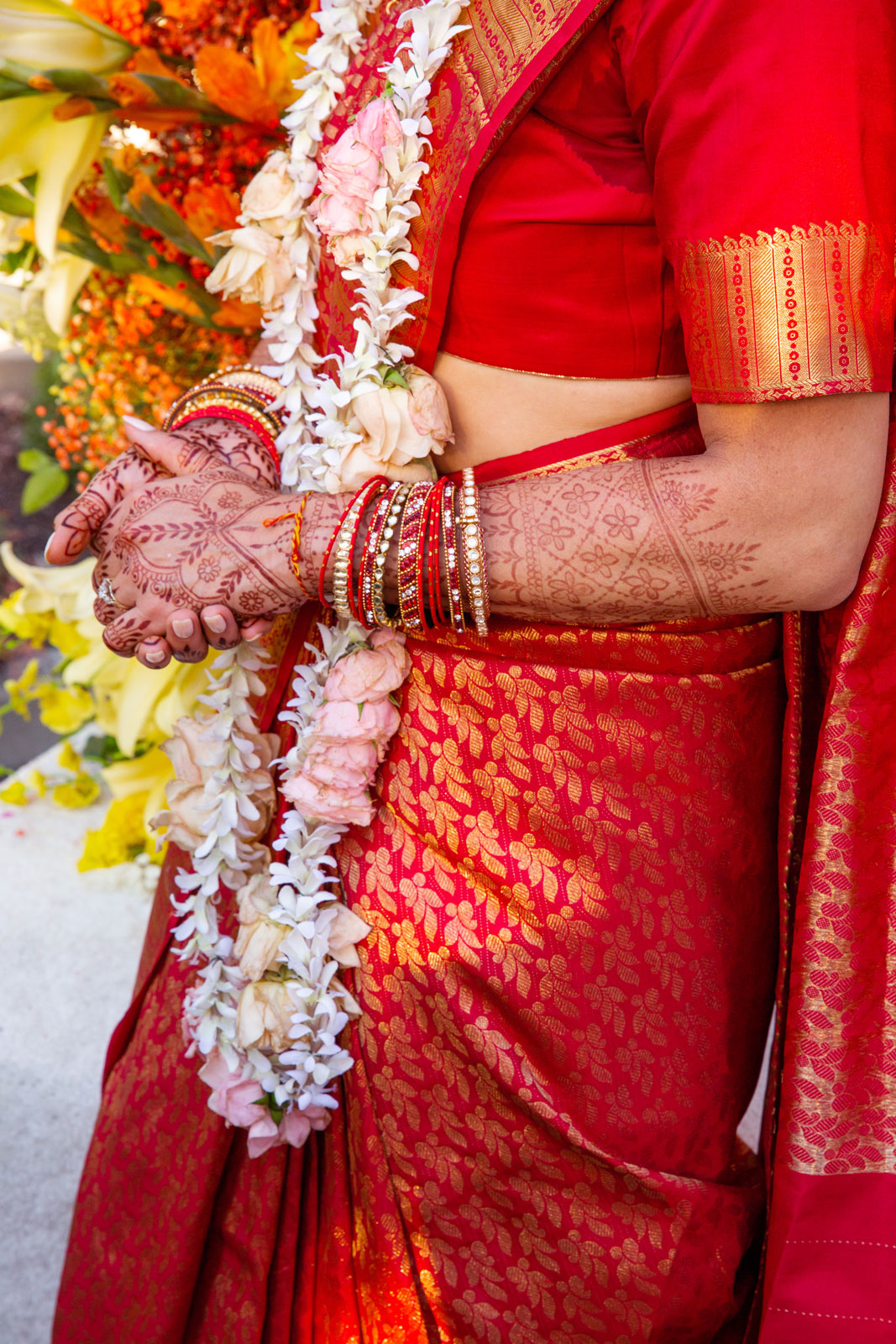 Close-up shot of the bride’s arms crossed at the wrists, showcasing her elaborate and beautifully detailed mehndi (henna tattoos) that cover her arms and hands.