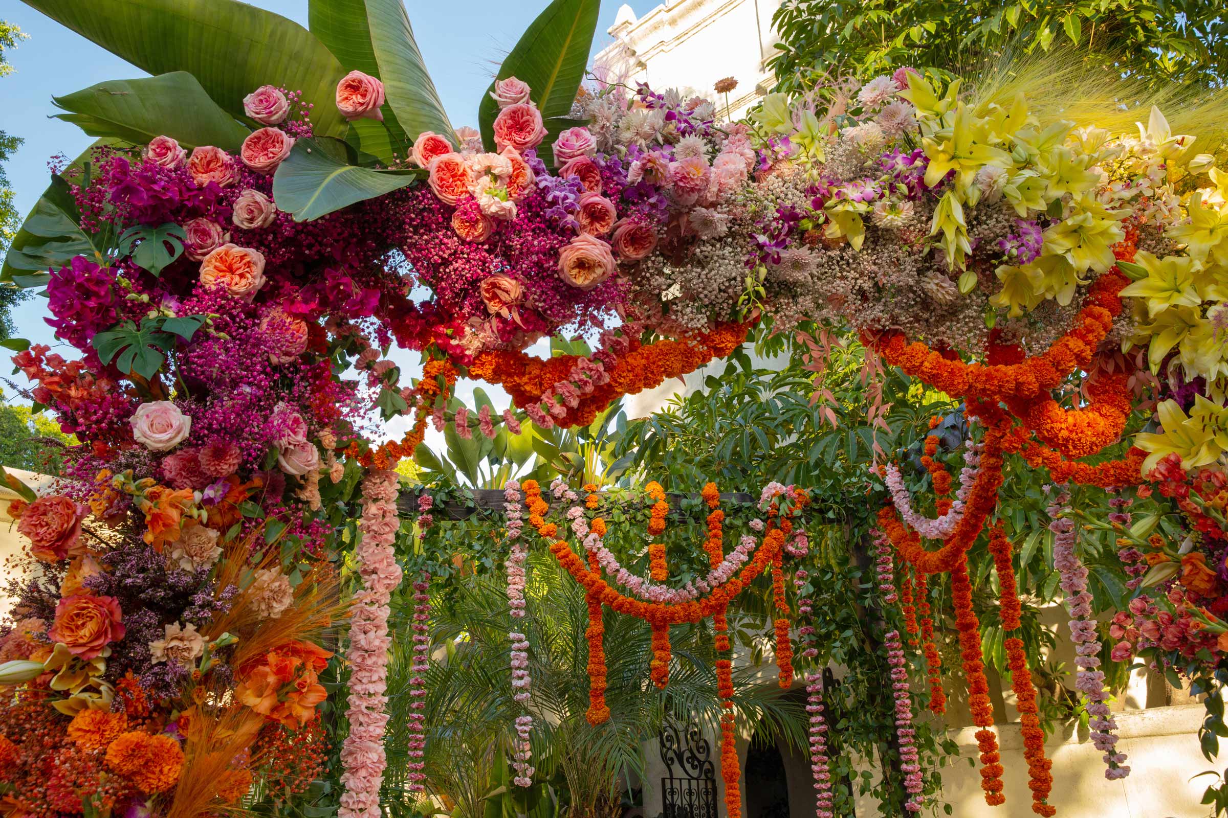 Close-up detail shots of A and H’s wedding mandap. The mandap is flanked by large tropical leaves and feathery yellow decorations, adding texture and a touch of whimsy to the floral arrangement.