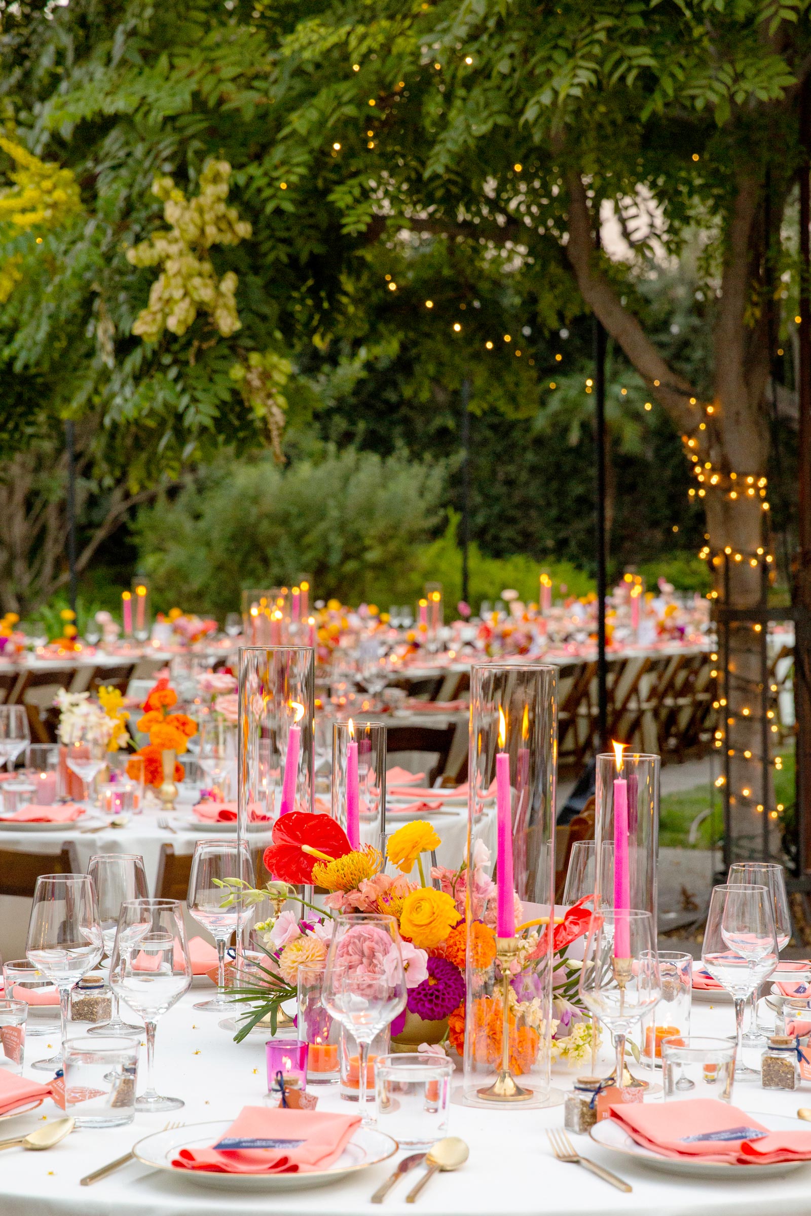 Another colorful reception shot of the tables. In the background, little string lights are seen hugging a tree, and you can see it becoming nighttime.