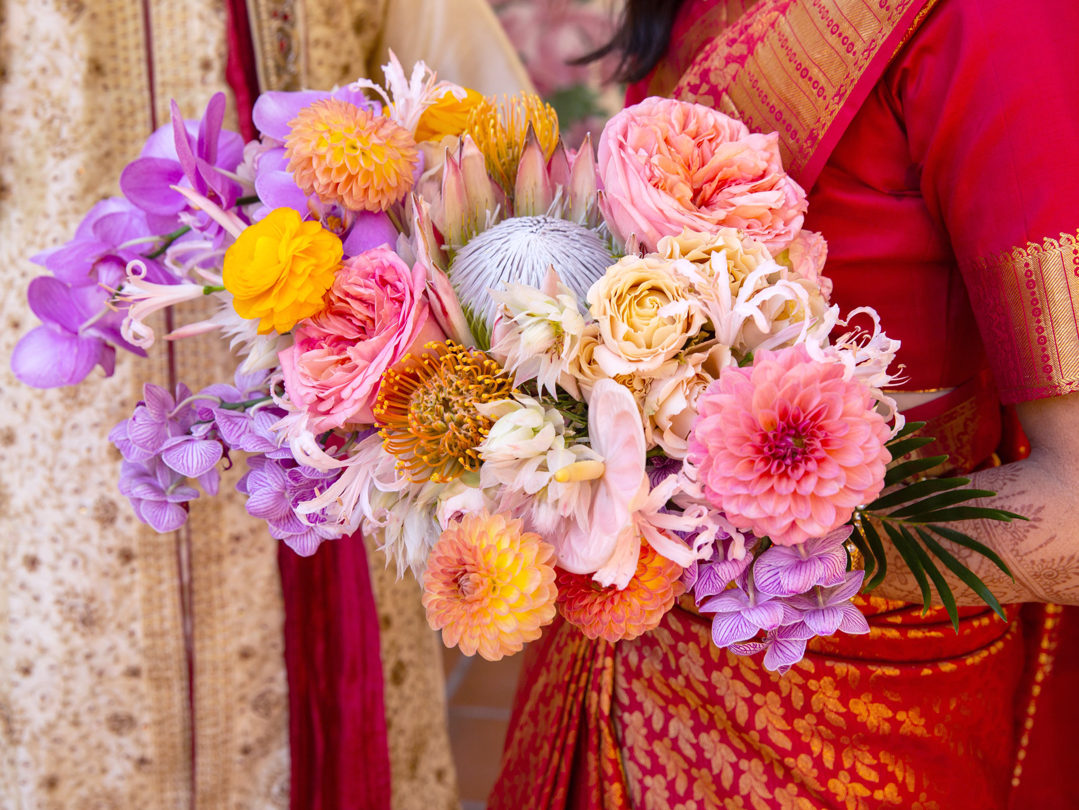 Close-up shot of A’s wedding bouquet, a colorful mix of flowers, including purple orchids, orange and pink roses, and other assorted blossoms.