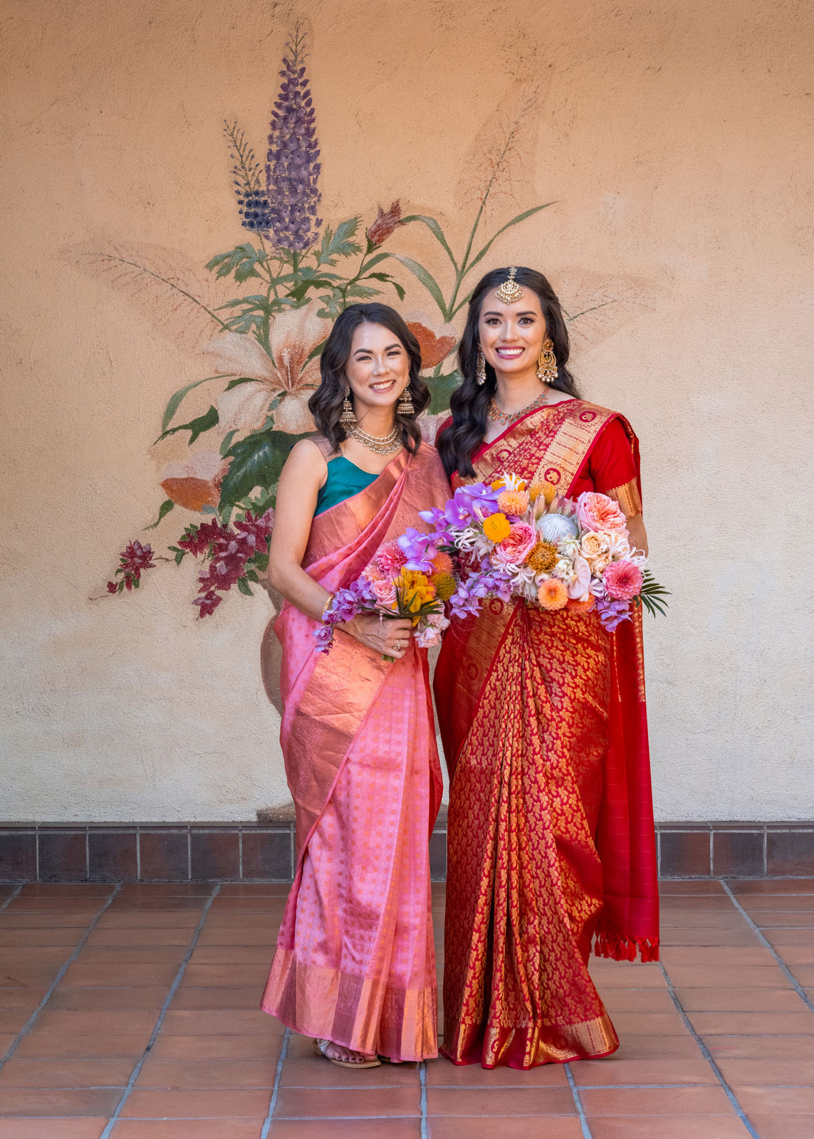 Full body portrait of A and her sister. Both are dressed in colorful, traditional Indian attire.