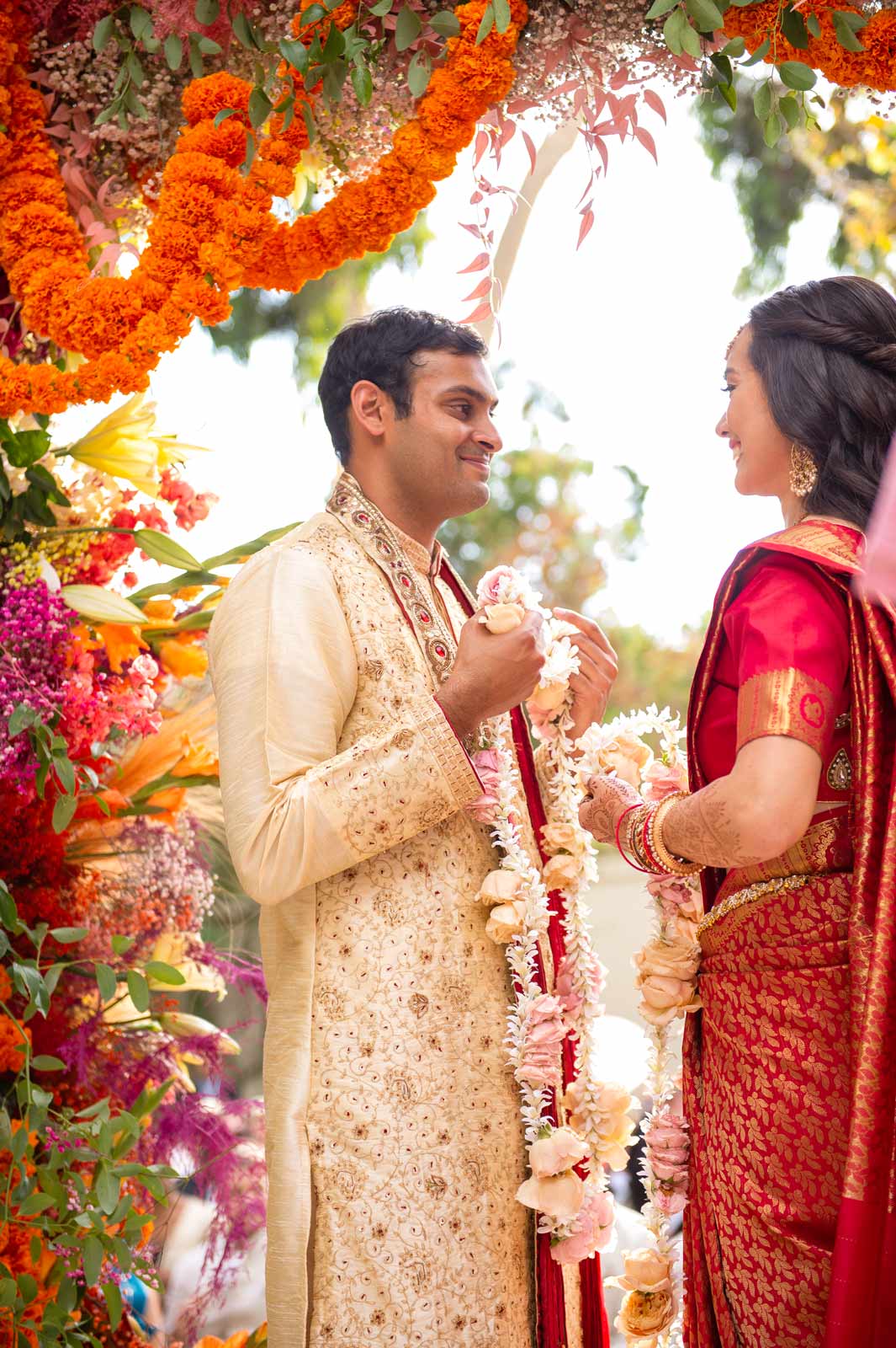 Another capture of the bride and groom facing each other, each holding ends of a floral garland, ready to place them around each other as a symbol of mutual respect and love.