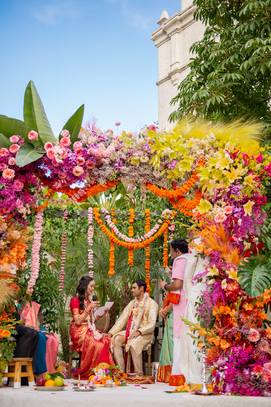 Another wide shot of the bride and groom seated under the floral mandap.