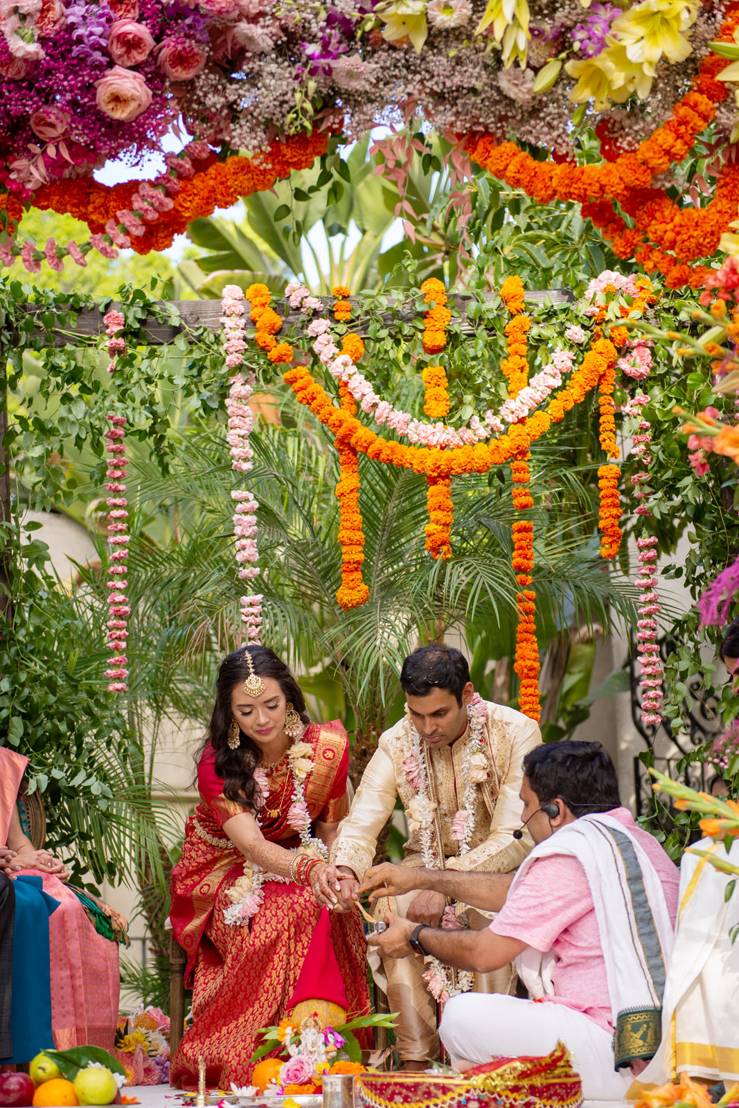 The next few shots are of the bride and groom seated under the ornate floral mandap, surrounded by an array of vivid flowers and green foliage.