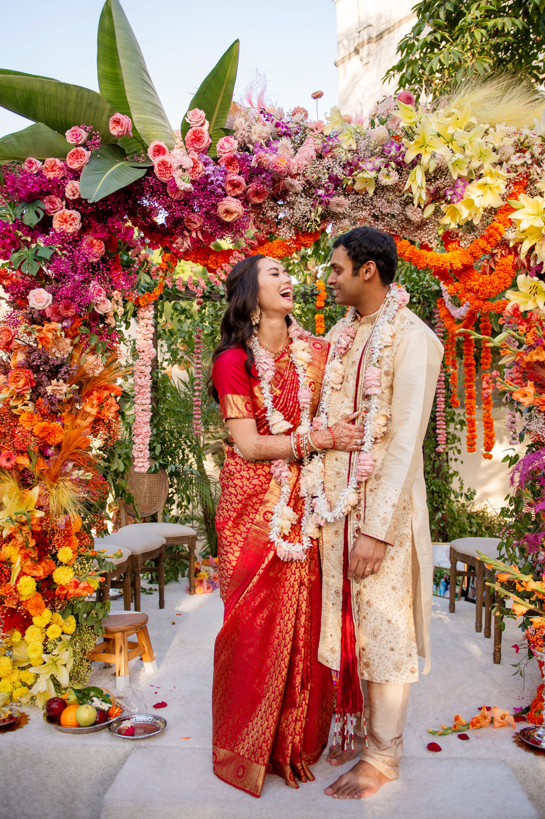 Full body portrait of A and H under the mandap, smiling at each other.