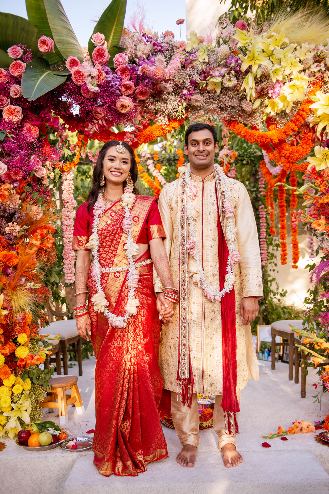 Full body portrait of A and H under the mandap smiling towards the camera