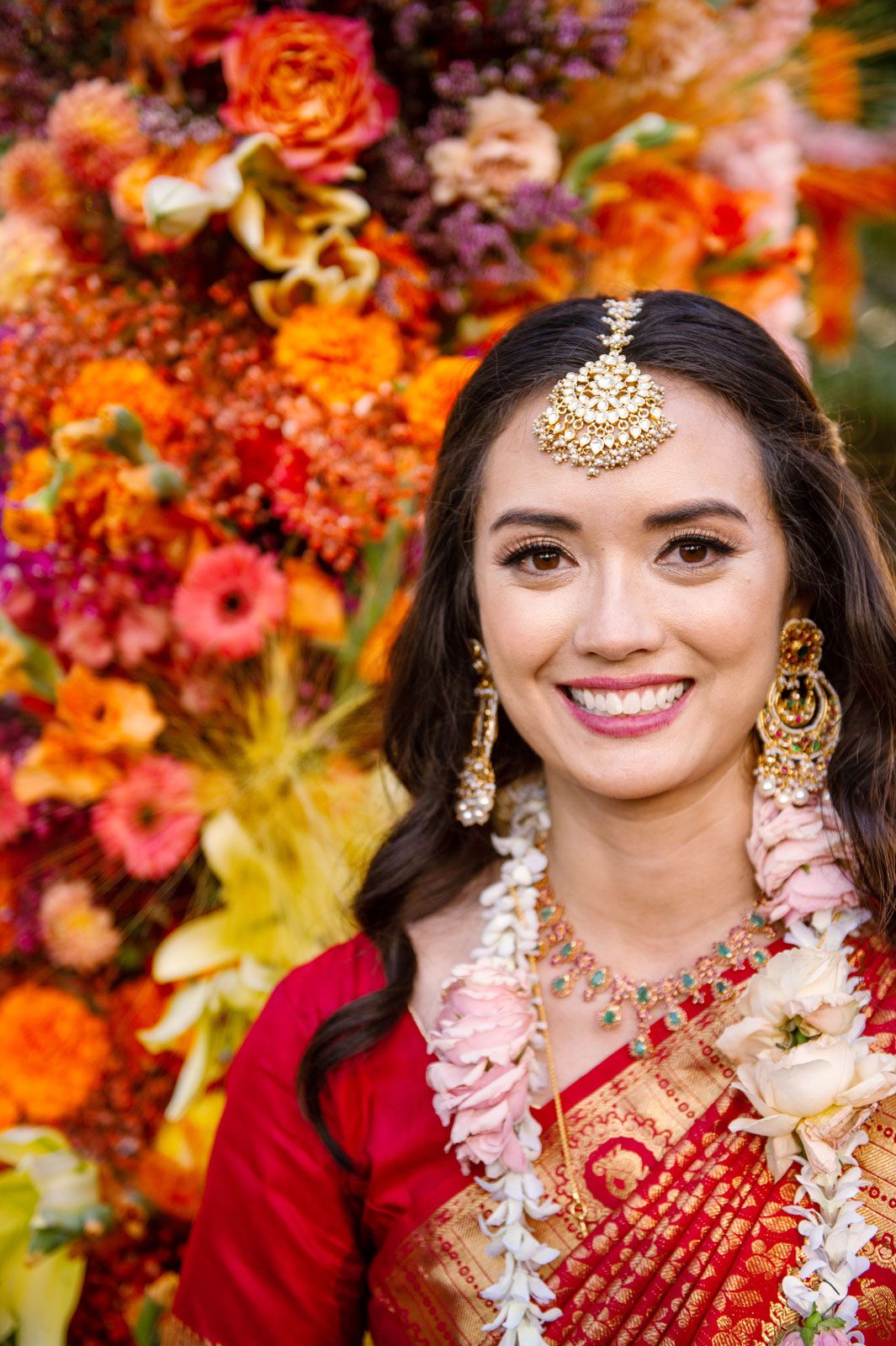 Medium shot of our bride in all her beauty with an ornate maang tikka on the top of her forehead, smiling into the camera