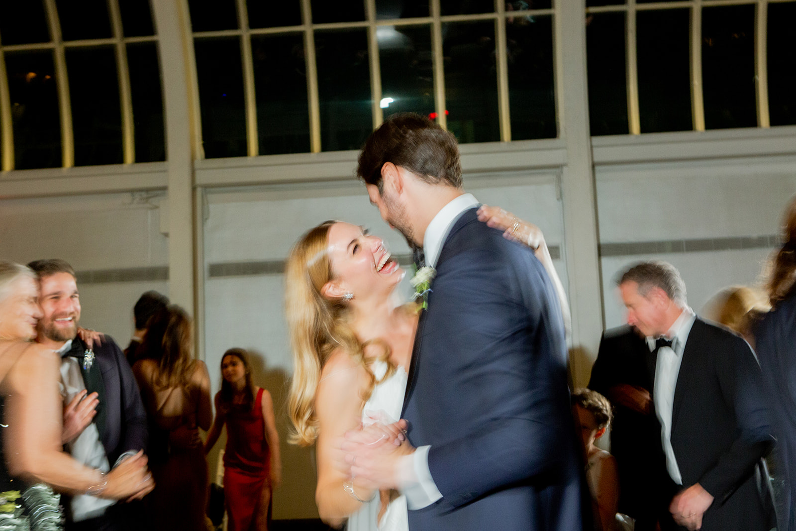 Candid moment between the newlyweds as they share a dance. The bride laughs with her head tilted back while the groom holds her close, smiling and completely immersed in the moment.