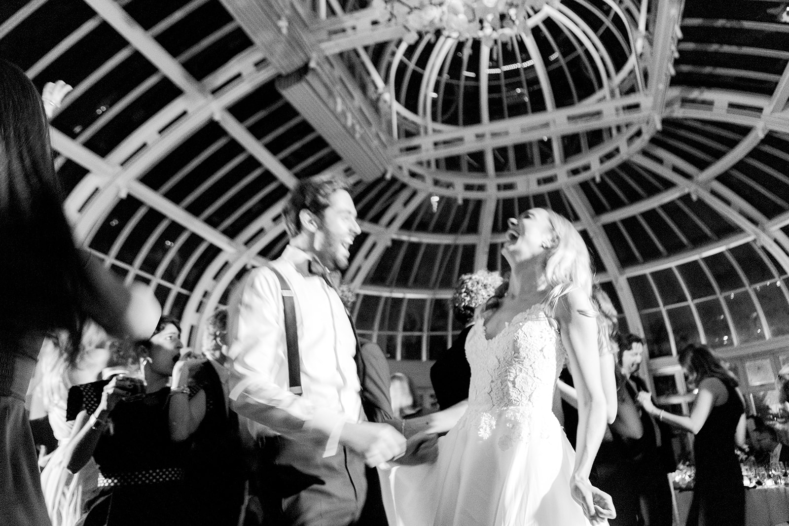 Black-and-white candid of the couple during a lively, joyous moment during the wedding reception. The bride and groom laugh and dance together, appearing carefree and fully immersed in the celebration.