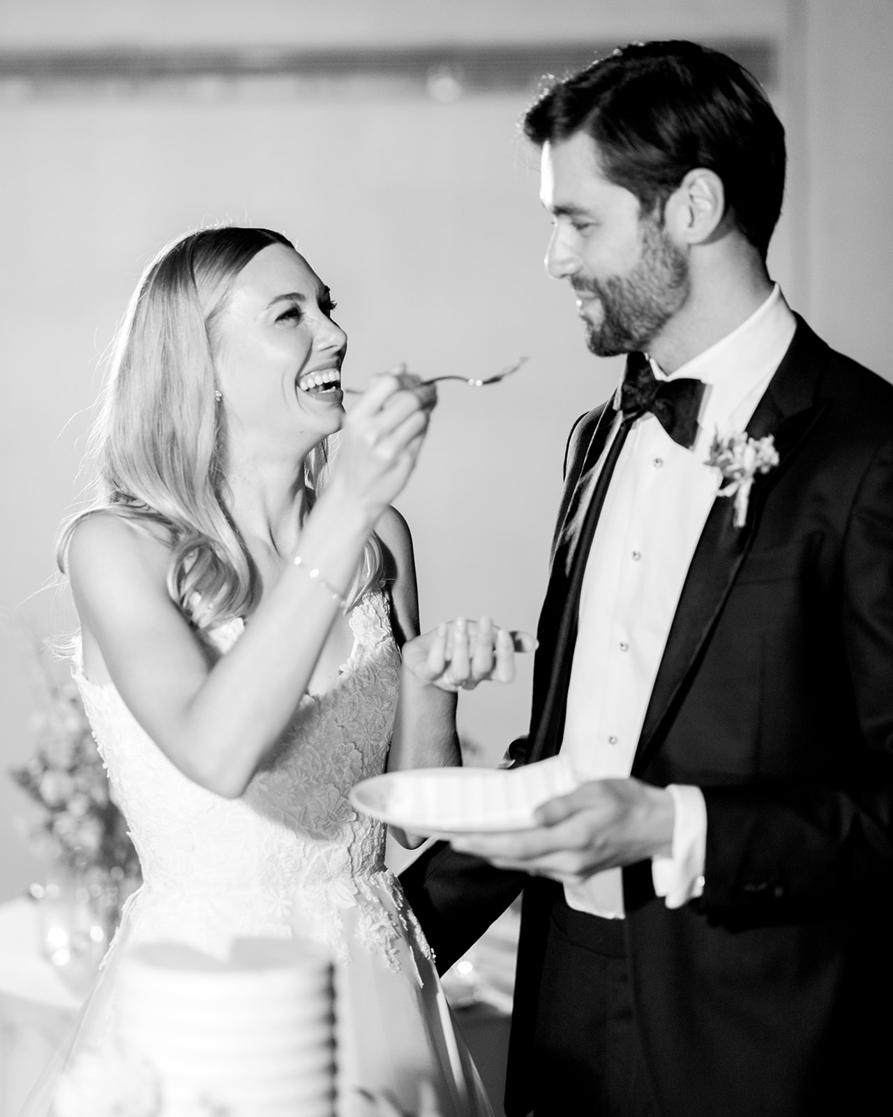 Black-and-white capture of the bride feeding the groom a bite of cake. It’s a joyful moment with a playful expression on the bride
