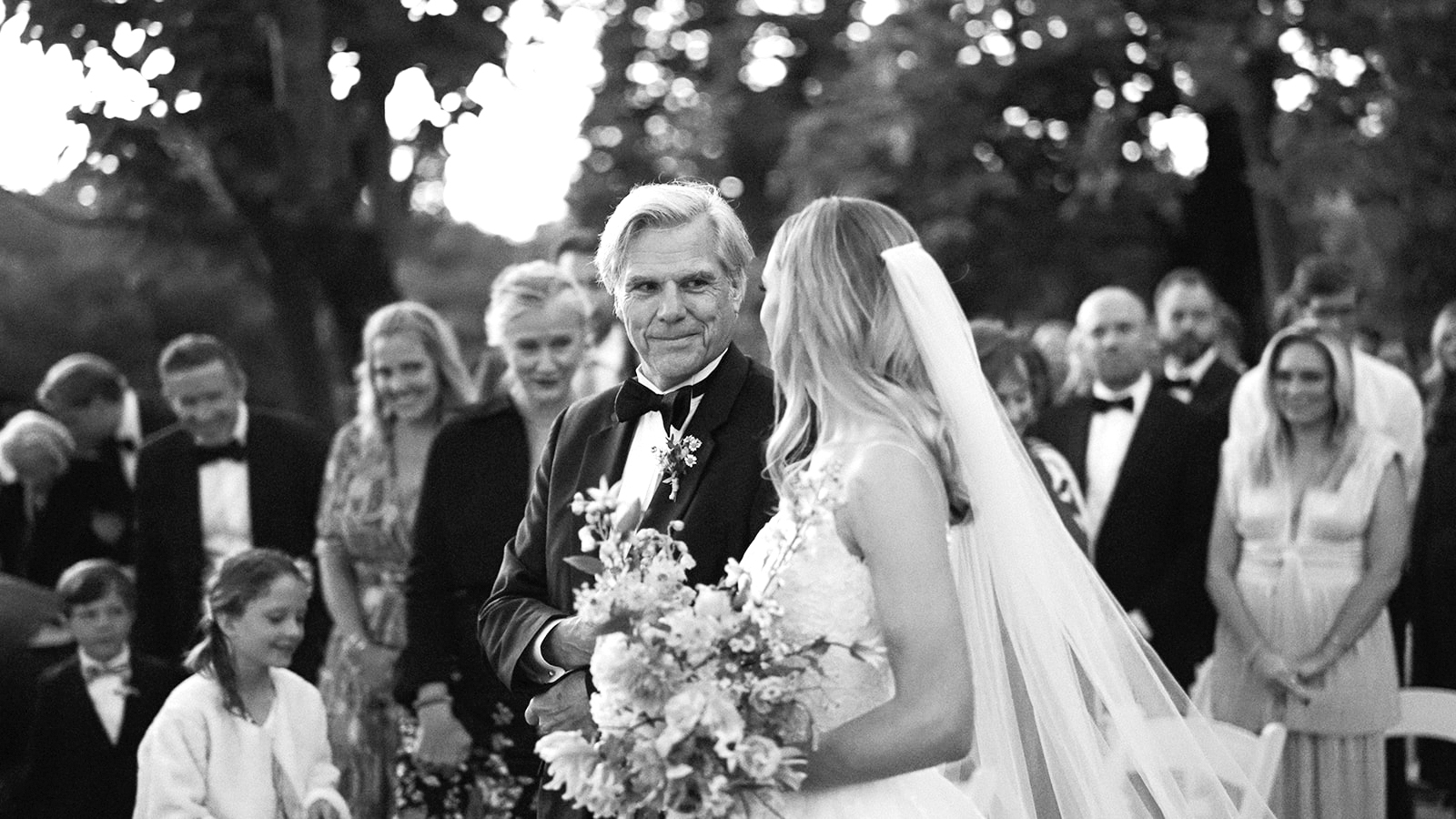 Black-and-white image of the bride being escorted down the aisle by her father.